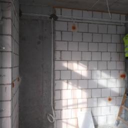 EL-BOL, Usługi Elektryczne, Smart Home - Surowy stan wnętrza w trakcie prac: białe kable poprowadzone po ścianach z bloczków, widoczne puszki instalacyjne, betonowy sufit, fragment drabiny i osoba w odblaskowej kamizelce w tle.