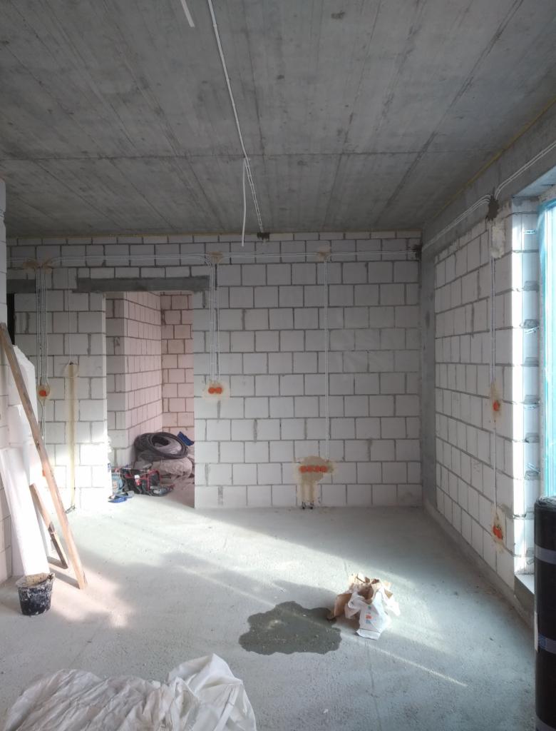 Surowy stan wnętrza w Dębowcu z widoczną instalacją elektryczną w peszlach na ścianach z betonu komórkowego i przewodami pod sufitem, przed tynkowaniem.