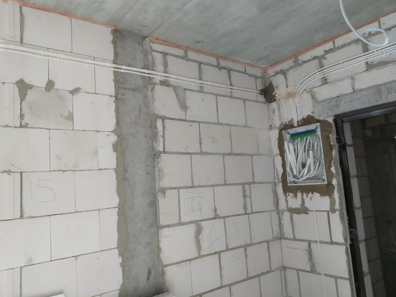 Surowy stan wnętrza z widocznymi przewodami elektrycznymi ułożonymi na ścianach z betonu komórkowego i puszką elektryczną z przewodami w ścianie.