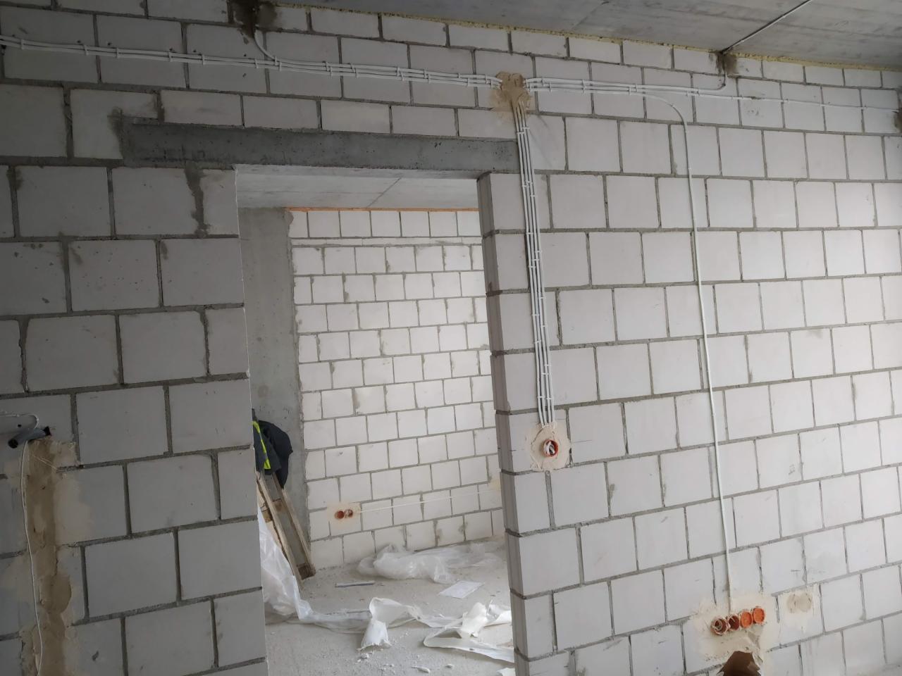 Surowy stan wnętrza z widocznymi kablami elektrycznymi prowadzonymi po ścianach z betonu komórkowego, instalacja podtynkowa w trakcie realizacji.