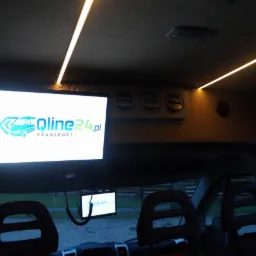 Wnętrze busa z zamontowanymi ekranami LCD wyświetlającymi logo firmy Qline24.pl Transport oraz oświetleniem LED podsufitki.
