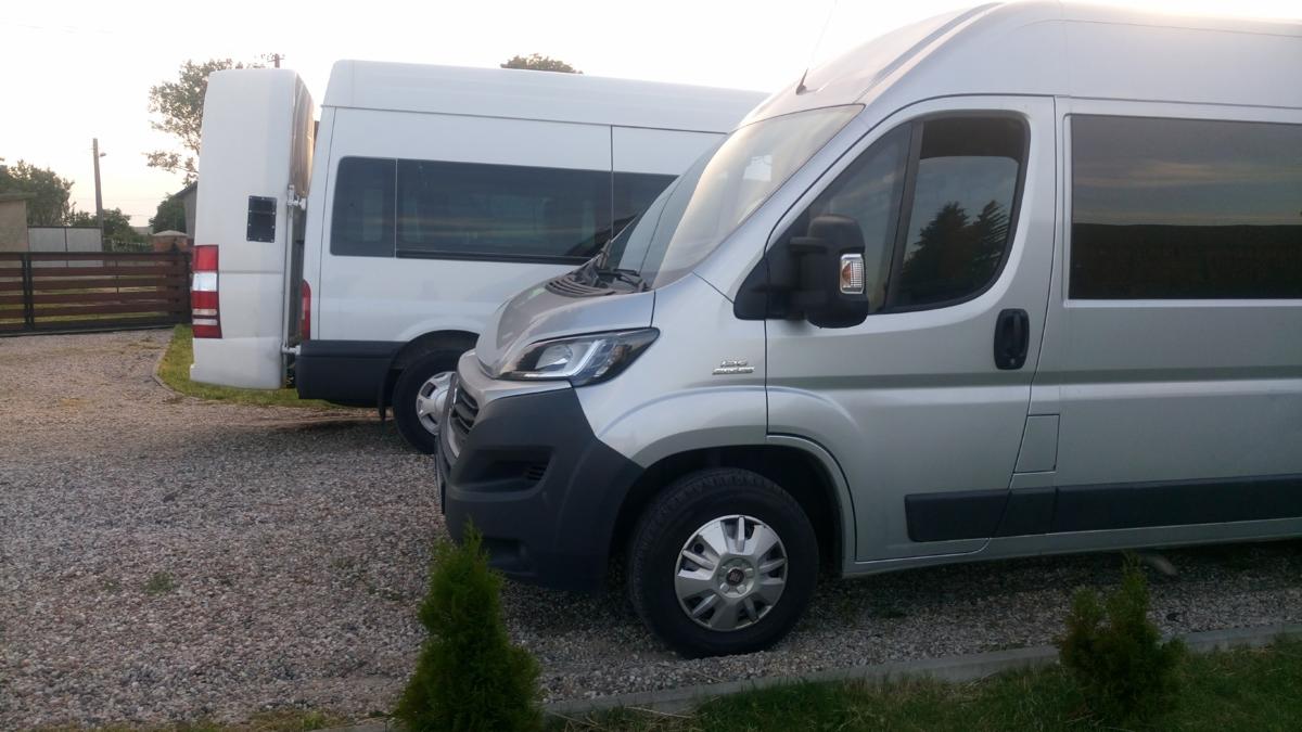 Dwa busy: srebrny Fiat Ducato z przodu i biały Mercedes Sprinter z otwartymi drzwiami z tyłu, stojące na żwirowym podjeździe.
