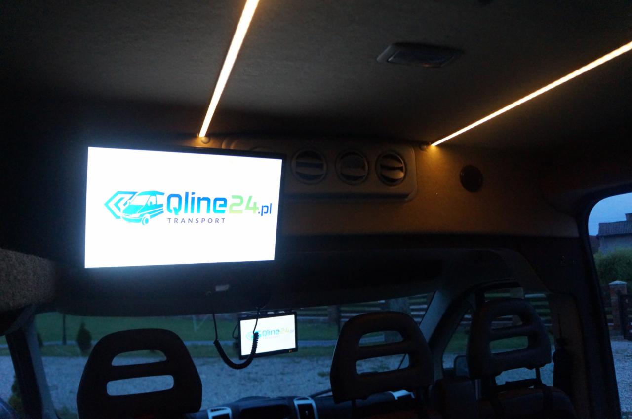 Wnętrze busa z zamontowanymi ekranami LCD wyświetlającymi logo firmy Qline24.pl Transport oraz oświetleniem LED podsufitki.