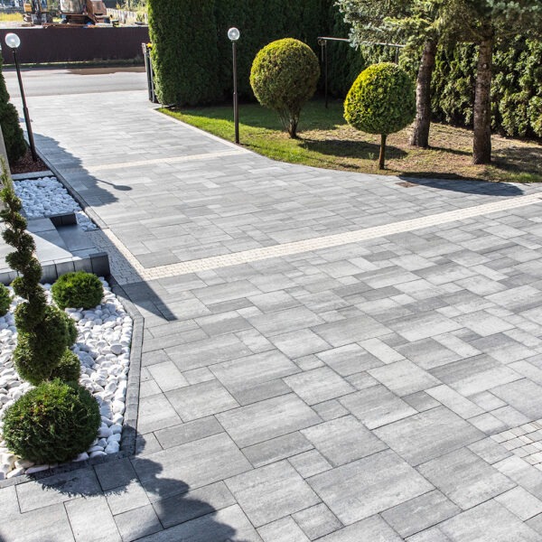 Szara kostka brukowa Pallazo ułożona na podjeździe z dekoracyjnym obramowaniem i elementami ozdobnymi z białych kamieni oraz zieleni. Widok z góry.