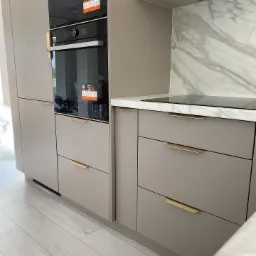 Nowoczesna kuchnia w odcieniach szarości z marmurowym backsplashiem, złotymi uchwytami i wbudowanym piekarnikiem.