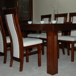 Ciemnobrązowy, drewniany stół jadalny z czterema krzesłami z jasną tapicerką, udekorowany drobnymi, białymi elementami dekoracyjnymi, na tle mebli w podobnym odcieniu drewna i jasnej ściany.