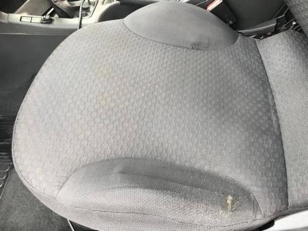 Szare, tekstylne siedzenie samochodowe z widocznymi śladami użytkowania i niewielkim uszkodzeniem tapicerki w dolnej części.