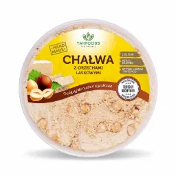 Okrągłe opakowanie chałwy z orzechami laskowymi marki Takfoods, z informacją o ręcznym wyrobie i braku oleju palmowego oraz syropu glukozowo-fruktozowego, widoczne orzechy laskowe i kawałki chałwy.