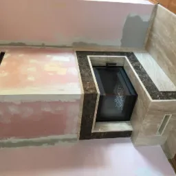 Wnęka kominkowa w trakcie wykańczania z użyciem beżowego i brązowego kamienia, widoczne niedoskonałości w postaci różowego podkładu i szczelin.