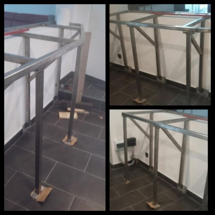 Konstrukcja metalowa z profili kwadratowych, prawdopodobnie w trakcie montażu, zabezpieczona kartonem u podstawy, widoczne ciemne płytki podłogowe i biała ściana.