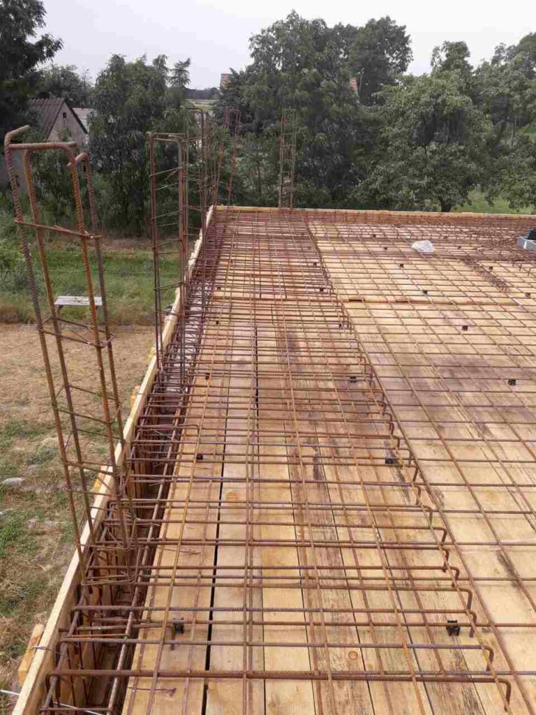 Zbrojenie stropu z wystającymi prętami na budowie domu jednorodzinnego, widok z góry na siatkę z drutu żebrowanego ułożoną na deskowaniu.