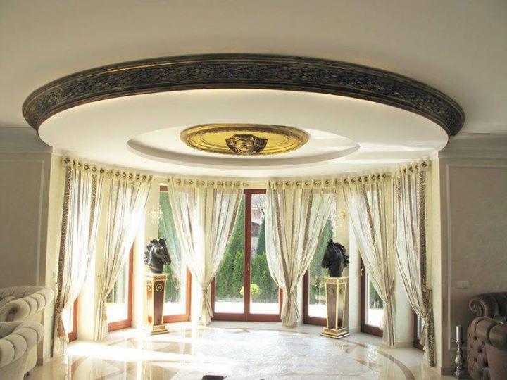 Luksusowe wnętrze z zaokrąglonym oknem, dekoracyjnym sufitem z ornamentami i rzeźbami końskich głów na postumentach, marmurowa podłoga.
