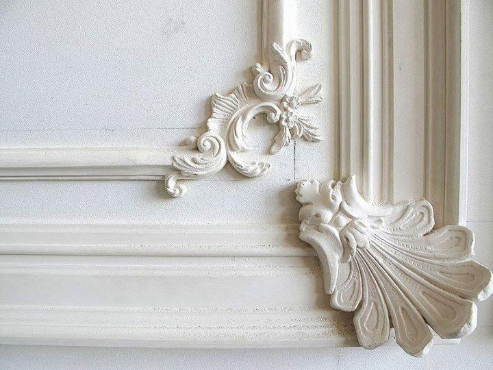 Białe, gipsowe zdobienia w stylu rokoko, częściowo przymocowane do ramy drzwi lub ściany z widocznymi śladami łączenia.