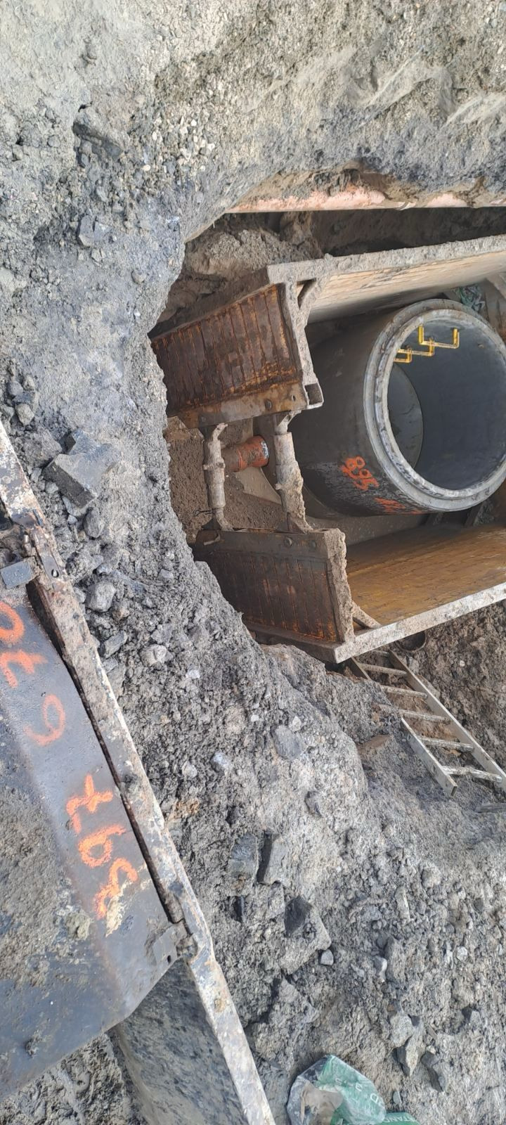 Wykop z widoczną rurą kanalizacyjną podtrzymywaną przez metalowe szalunki i drabinką ze stali nierdzewnej, ziemia wokół wykopu.