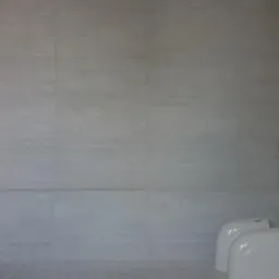 Szare, poziomo ułożone płytki ceramiczne na ścianie łazienki, widoczne dwie białe spłuczki podtynkowe w rogu oraz kartony z armaturą.