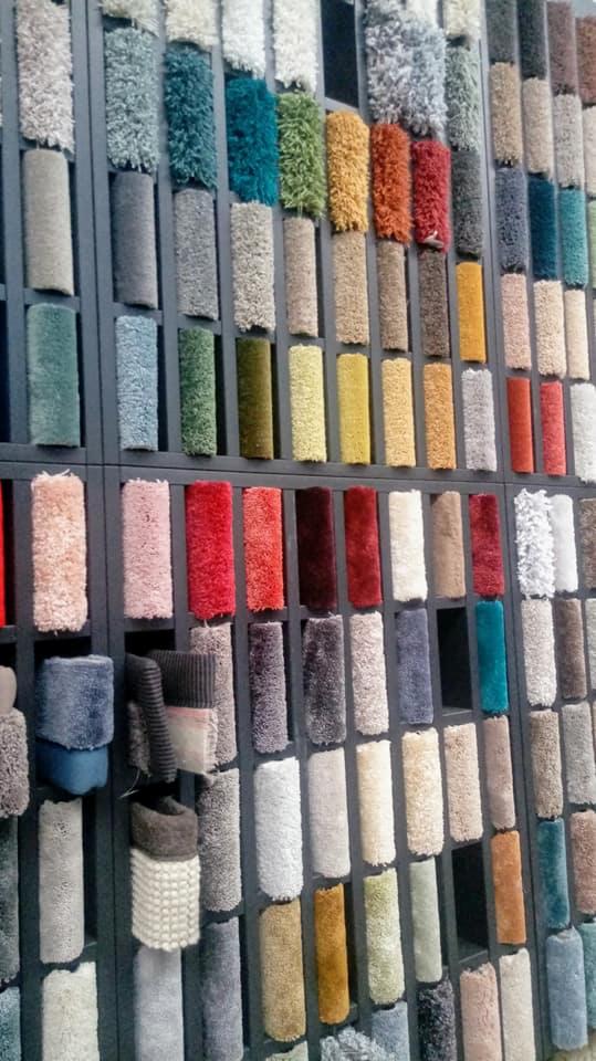 Ekspozycja próbek dywanów o różnorodnych kolorach i fakturach, umieszczonych na metalowym stelażu w sklepie.