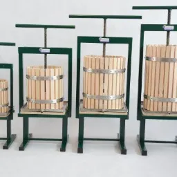 Cztery prasy do owoców o różnej pojemności, wykonane z drewna i metalu, ustawione w rzędzie na białym tle, prezentujące skalę rozmiarów.