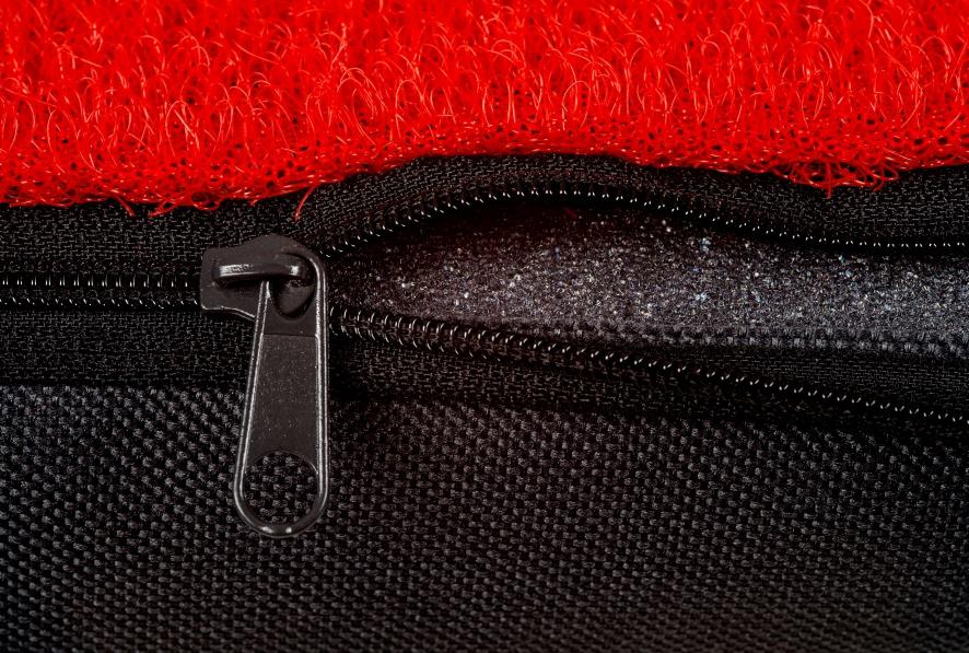 Czarne, teksturowane opakowanie z suwakiem, częściowo zakryte czerwoną, włóknistą tkaniną