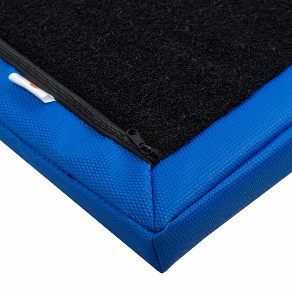 Fragment kwadratowej poduszki z czarną, teksturowaną powierzchnią i niebieskim, teksturowanym brzegiem, z widocznym zamkiem błyskawicznym i małą, białą etykietą.