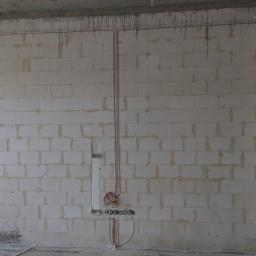 Elgrom - Wnętrze w trakcie instalacji elektrycznej: widoczne kable prowadzone po ścianie z białych bloczków, puszki pod gniazdka i włączniki, oraz otwór w suficie na oświetlenie.