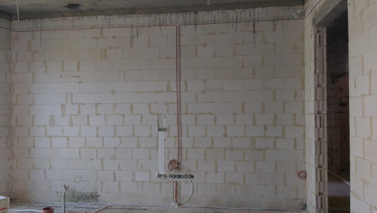 Wnętrze w trakcie instalacji elektrycznej: widoczne kable prowadzone po ścianie z białych bloczków, puszki pod gniazdka i włączniki, oraz otwór w suficie na oświetlenie.