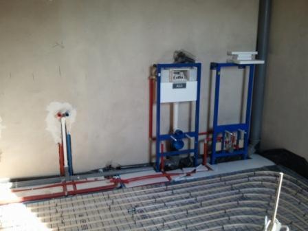 W trakcie montażu ogrzewania podłogowego w Koszalinie, widoczne rury grzewcze ułożone na podłodze oraz elementy instalacji sanitarnej i stelaże podtynkowe.