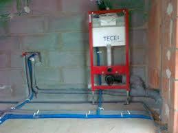 Stelaż podtynkowy WC marki TECE zamontowany na surowej ścianie z betonu komórkowego, z widocznymi niebieskimi rurami doprowadzającymi wodę, przymocowanymi do podłoża białymi uchwytami.