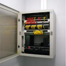 Otwarta szafa rack z uporządkowanymi kablami sieciowymi w kolorach czerwonym i żółtym, widoczne urządzenia sieciowe i listwa zasilająca.