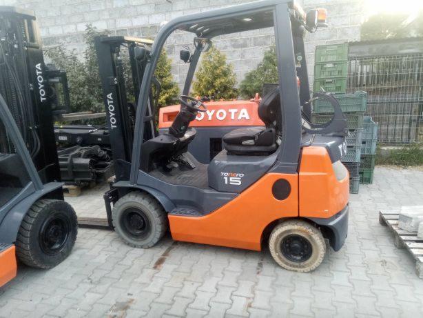 Pomarańczowo-szary wózek widłowy Toyota Tonero 15 na zewnątrz, z widocznymi paletami i skrzynkami w tle.