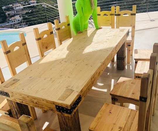 Rustykalny drewniany stół z krzesłami z metalowymi zdobieniami, wykonany na tarasie w Olsztynku z widokiem na wzgórza i basen.