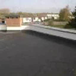 Wykończona, płaska powierzchnia dachu pokryta czarną papą termozgrzewalną, widok z góry na budynki mieszkalne w tle.