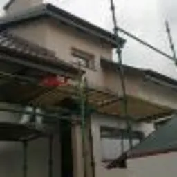 Dom w trakcie prac elewacyjnych, widoczne rusztowania, świeżo otynkowana ściana w jasnym odcieniu, częściowo zakryte okno, pochmurne niebo w tle.