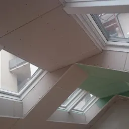 Montaż płyt karton gips na poddaszu wokół okien dachowych, widoczne szpachlowane łączenia i zielona izolacja.