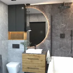 Nowoczesna łazienka z okrągłym lustrem podświetlanym LED, umywalką nablatową na szafce z drewnianymi frontami, szarą armaturą i pralką z lewej strony.