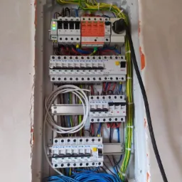 Rozdzielnica elektryczna wnękowa w stanie surowym, widoczne zabezpieczenia, przewody kolorowe i listwy zaciskowe. Jeden z wyłączników posiada zieloną diodę sygnalizacyjną.