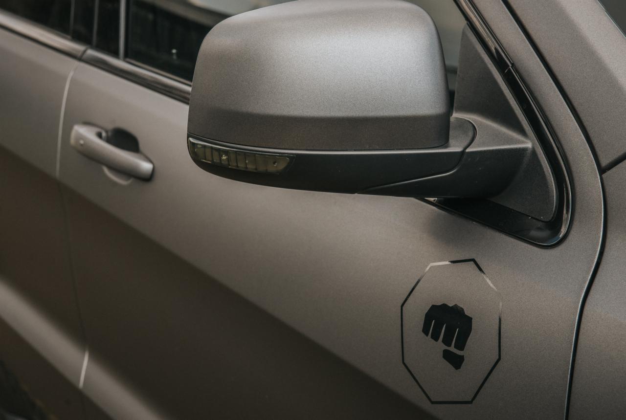 Matowy lakier na samochodzie z naklejką przedstawiającą zaciśniętą pięść w ośmiokącie, widoczne lusterko i klamka.