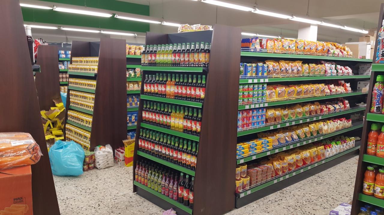 Widok na sklep spożywczy w Kielcach z nowymi, brązowymi regałami sklepowymi z zielonymi akcentami, wypełnionymi różnorodnymi produktami, od napojów po słodycze. Na podłodze widoczne worki i kartony.