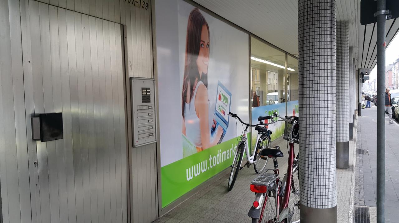 Reklama zewnętrzna sklepu Todimarkt z wizerunkiem kobiety z laptopem, zaparkowane rowery przy ścianie budynku.