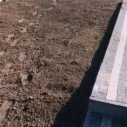 Przygotowanie terenu pod budowę ogrodzenia w Skrzeszewie Żukowskim, widoczne wyrównane podłoże i pracownik z narzędziem w tle, obok ułożona kostka brukowa.