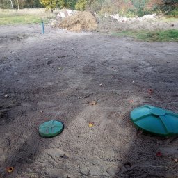 EKO-FASS Krzysztof Różnicki - Dwa zielone włazy szamba betonowego na ziemi w Witkowie. W tle widać pryzmę piasku i drzewa. Ślady stóp na ziemi sugerują niedawne prace.