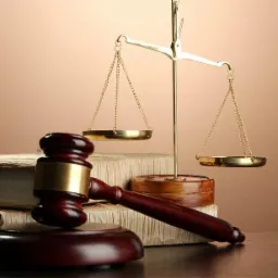 Drewniany młotek sędziowski i złote wagi sprawiedliwości na tle stosu starych ksiąg prawniczych.