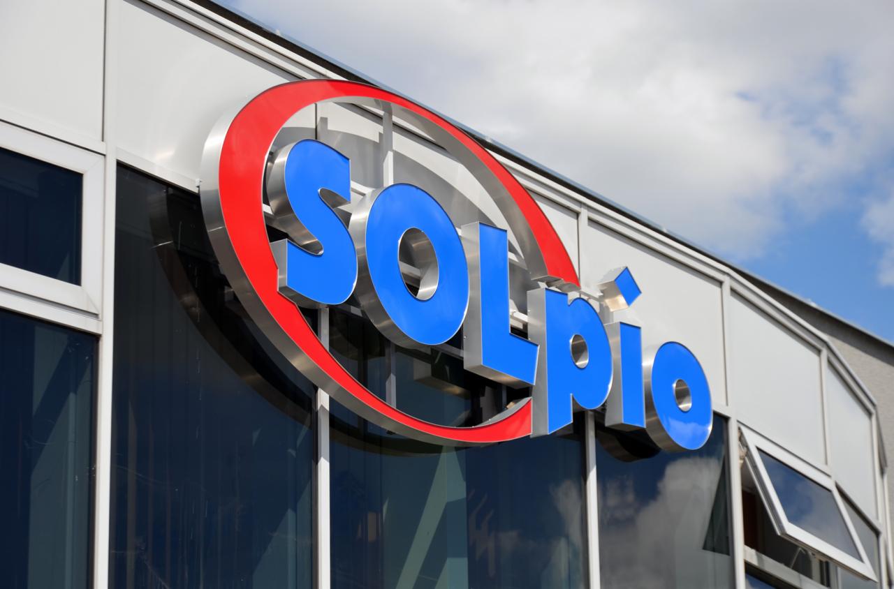 Zewnętrzny znak firmy Solpio z niebieskimi literami i czerwonym okręgiem na elewacji budynku z oknami.