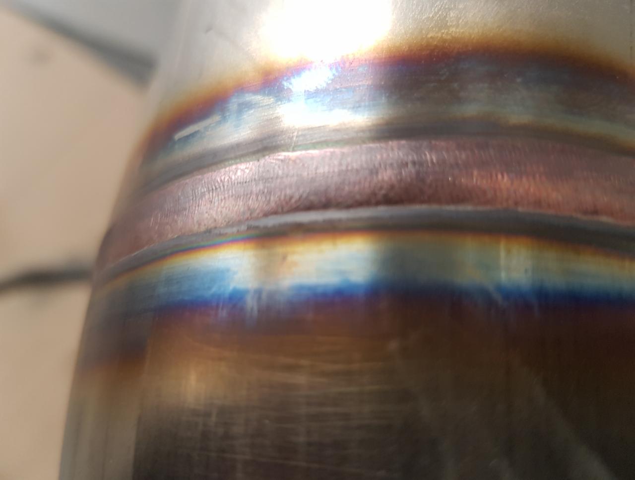 Zbliżenie na spoinę na rurze ze stali nierdzewnej, widoczne tęczowe przebarwienia termiczne.