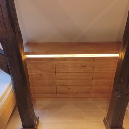 WoodMood Design Adam Pańkow - Szafa wkomponowana w skos dachu z drewnianymi belkami konstrukcyjnymi, oświetlona listwą LED, widok z dołu, sypialnia na poddaszu.