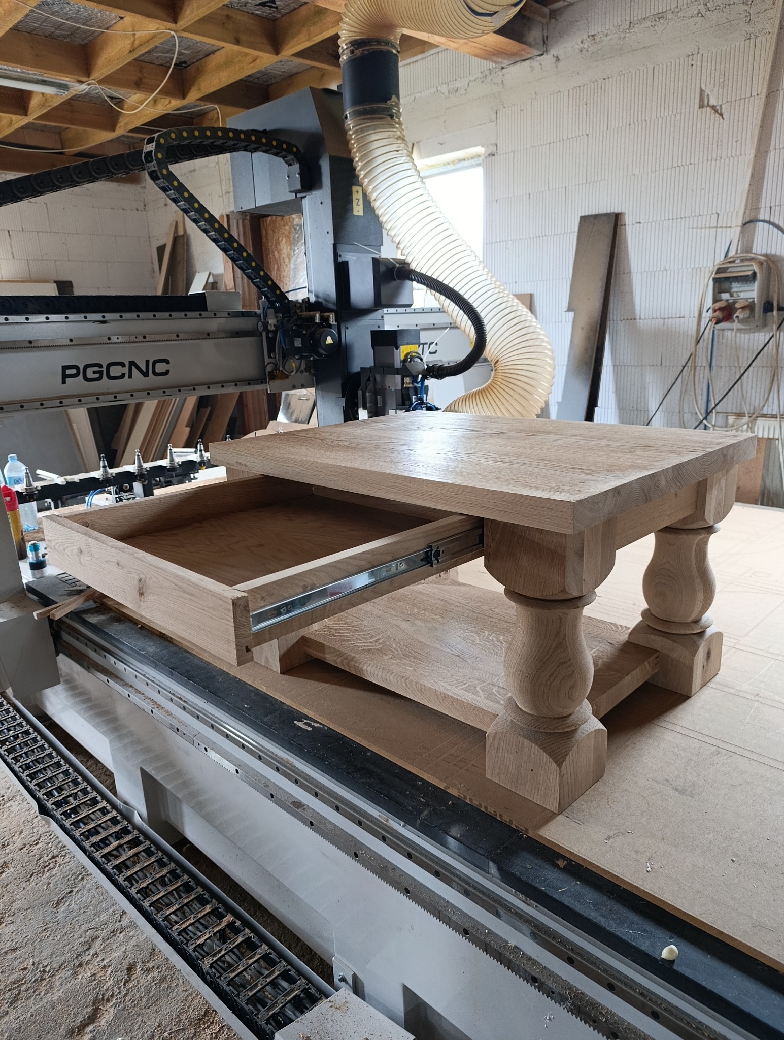 Drewniany stolik kawowy z wysuwaną szufladą, w trakcie produkcji na frezarce CNC PGCNC. Widoczne detale toczonych nóg i surowe drewno.