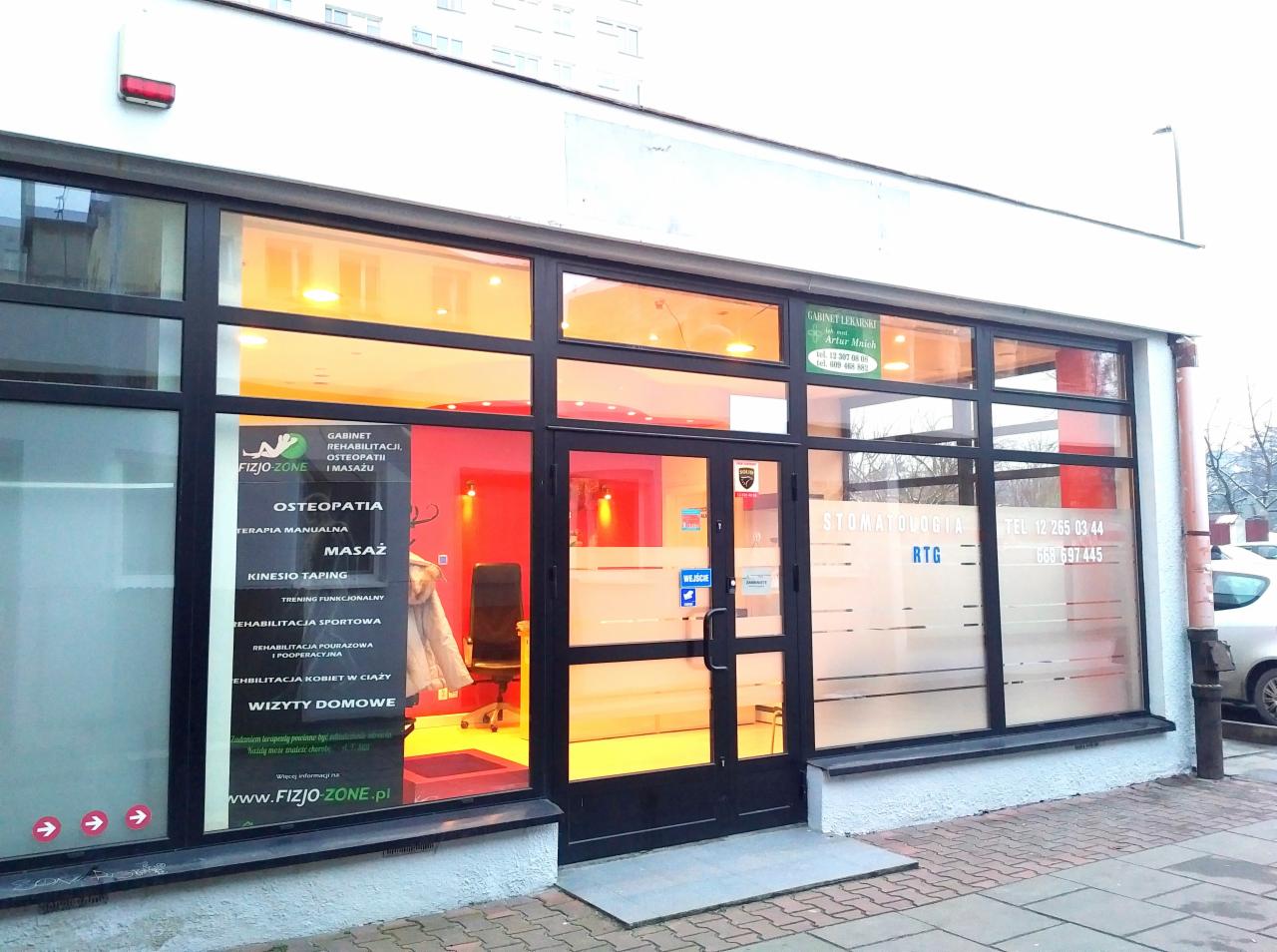 Fasada budynku z gabinetami rehabilitacji, osteopatii, masażu oraz stomatologii, widoczne szyldy informacyjne i numery telefonów.