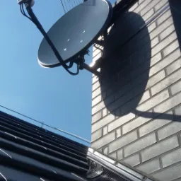 Antena satelitarna i antena naziemna zamontowane na kominie z cegły, widok z dołu na tle błękitnego nieba.