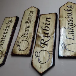 Ręcznie robione, wypalane deski z nazwami odmian jabłek (Anton&oacute;wka, Szara Reneta) i gruszek (Rubin, Łukas&oacute;wka), drewno opalane, lakierowane, widoczne słoje.