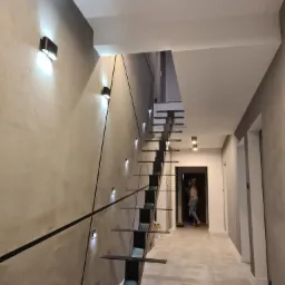 Nowoczesne schody wspornikowe z czarnymi elementami i oświetleniem LED w szarej klatce schodowej z osobą w tle.