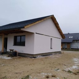 Jak zrobię, Tak Będzie usługi ogólnobudowlane Mariusz Malicki - Dom jednorodzinny z nową, ciemną dachówką i jasną elewacją w trakcie wykańczania, widoczne rusztowania i materiały budowlane na posesji.